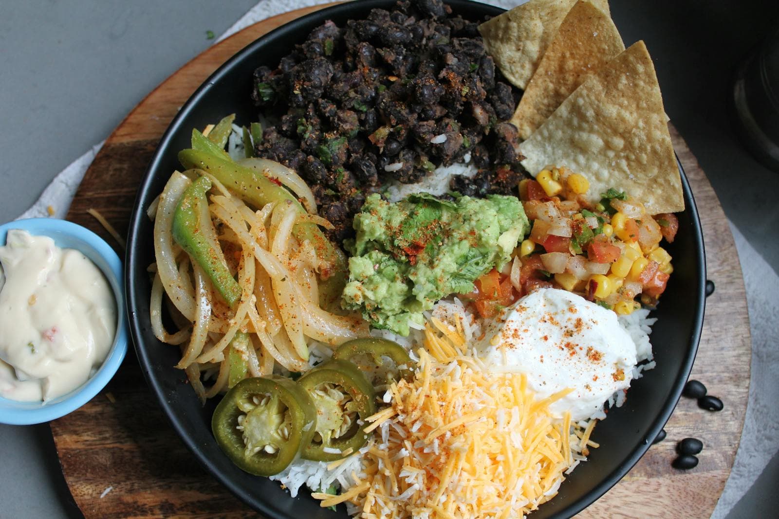 A colourful burrito bowl with guacamole, beans, and shredded cheese