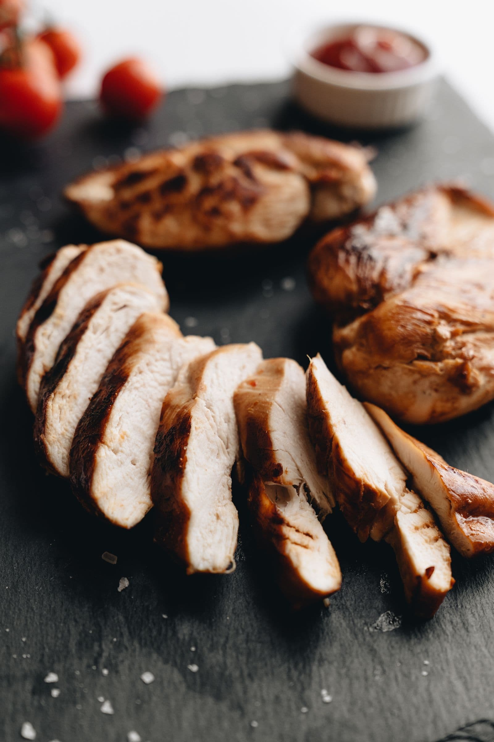 Sliced grilled chicken breast on a slate board with tomato garnish